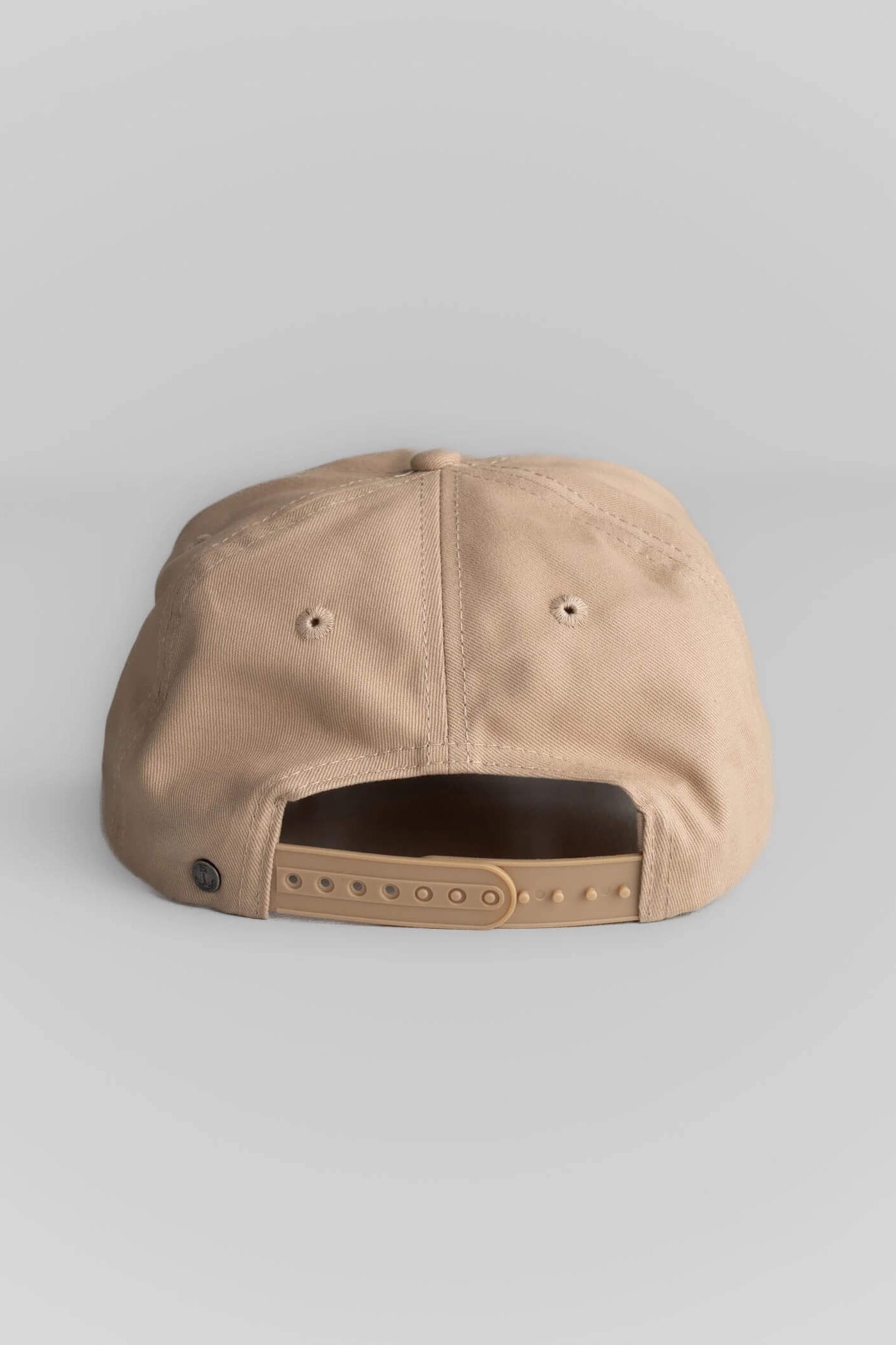 A beige snapback cap shown from the back, featuring a structured fabric crown, two ventilation eyelets, and an adjustable hook-and-loop strap closure on a light gray background.