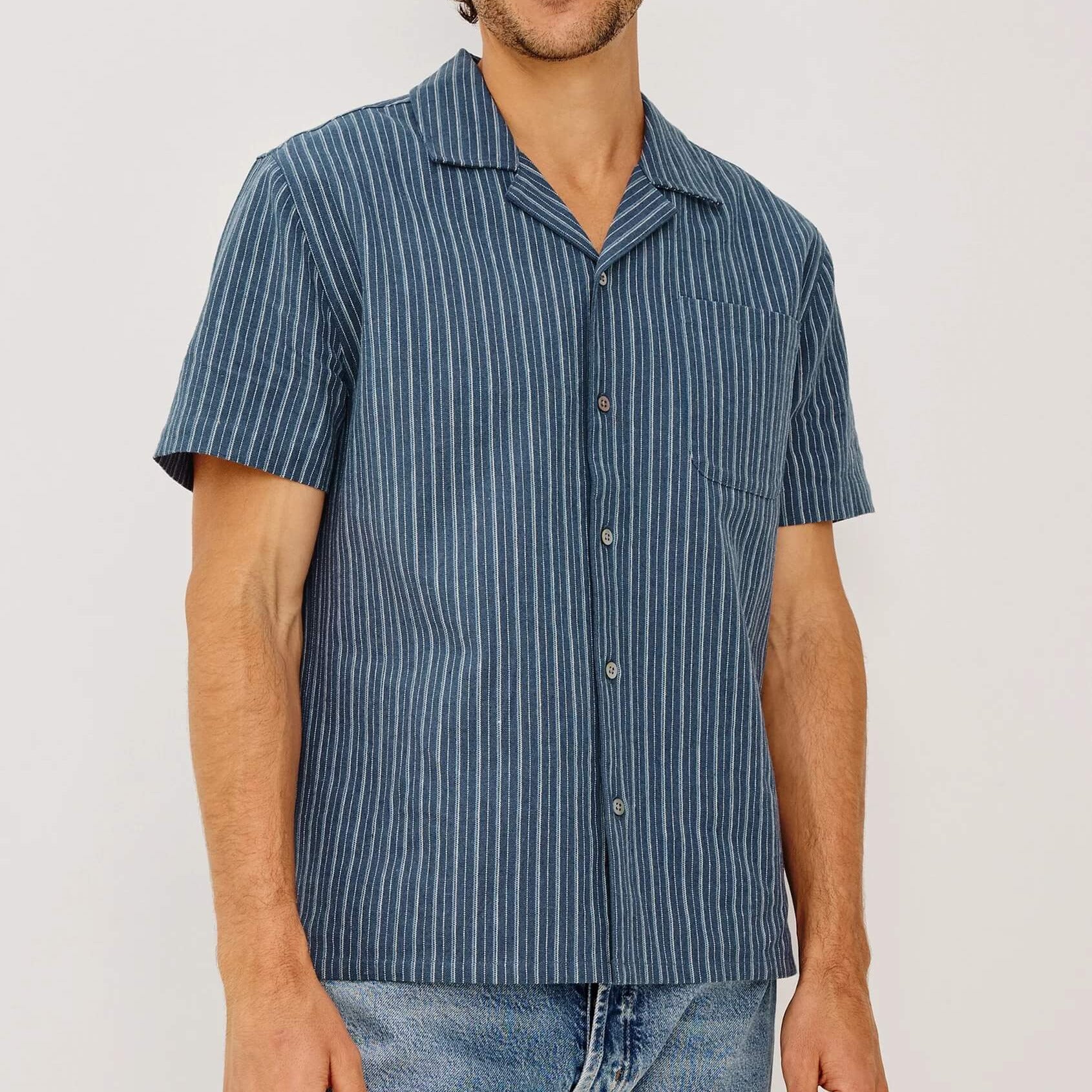 Man wearing a blue striped shirt and jeans against a plain background