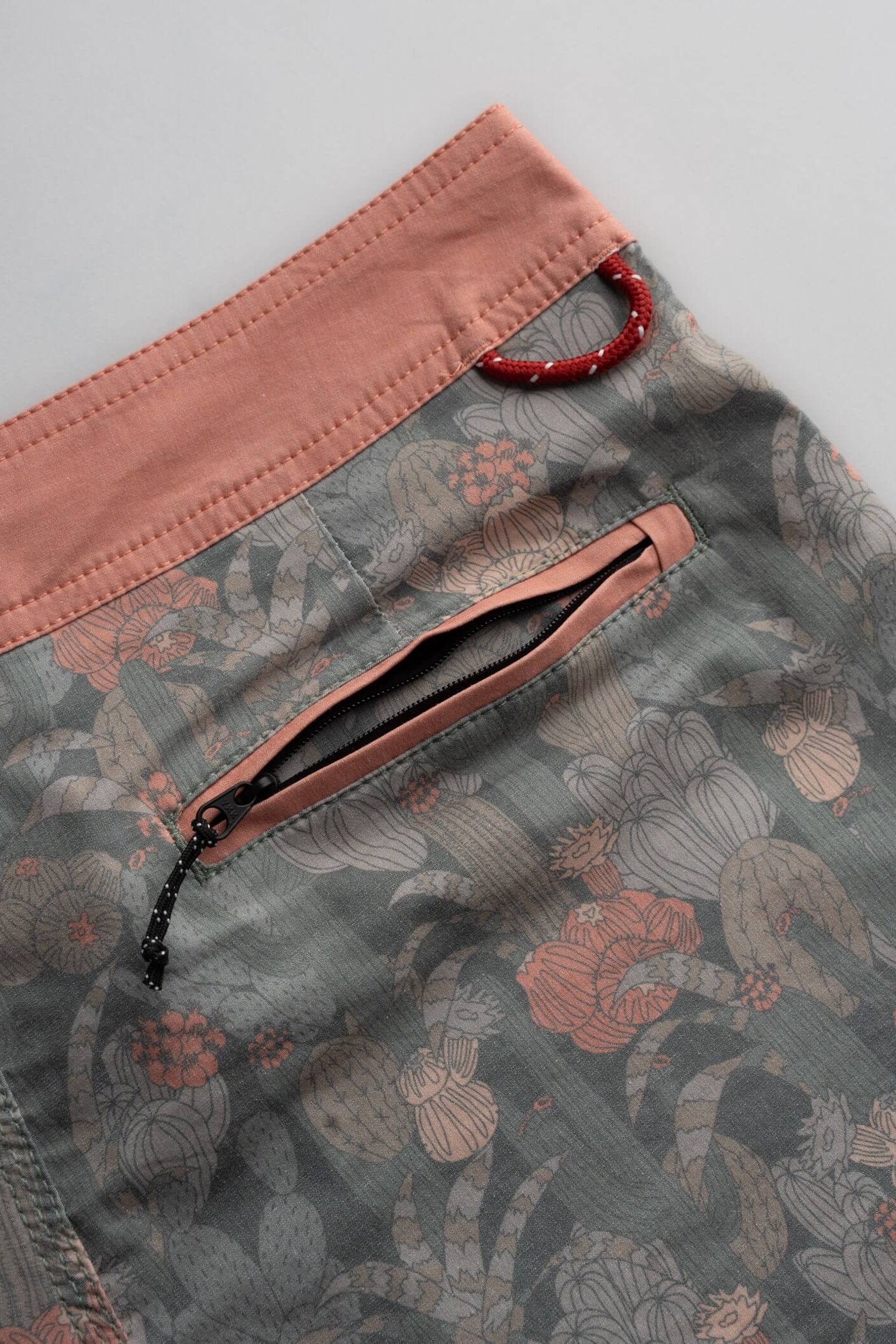 Close-up of a pair of shorts showing a dusty gray floral pattern, a contrasting dusty pink waistband, and a matching zippered pocket.
