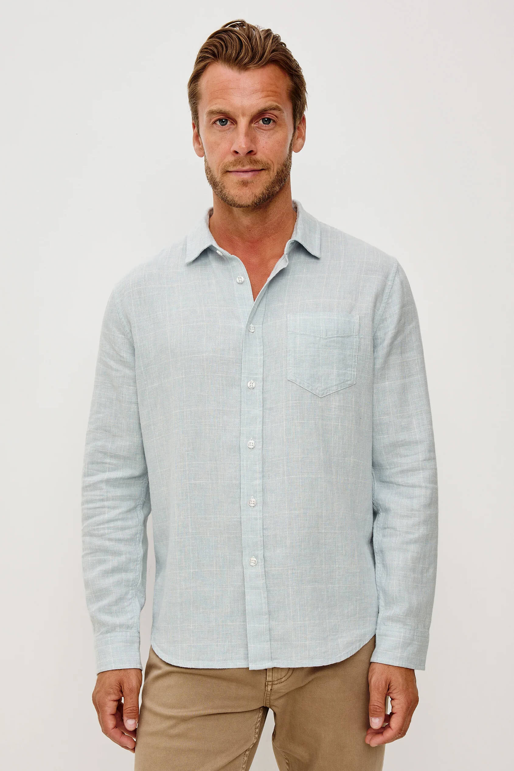Man wearing a light blue striped shirt and beige pants on a white background